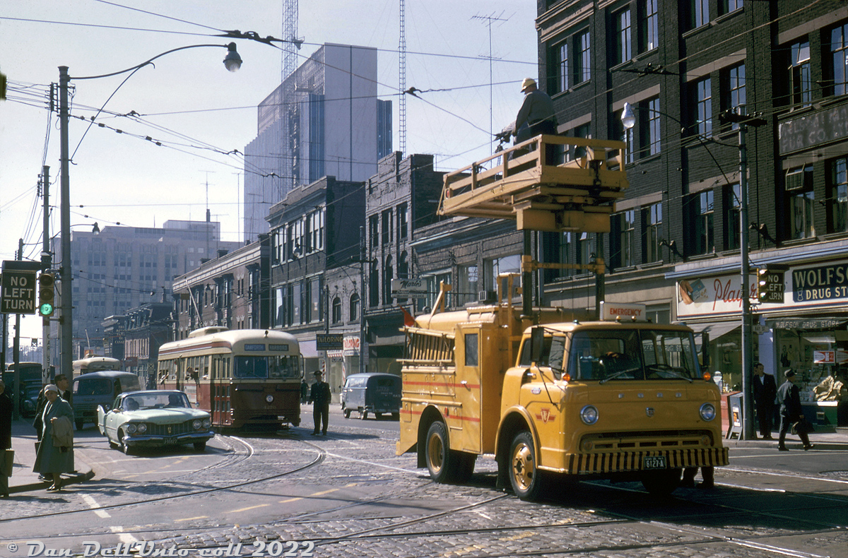 There's a bit of a delay at the busy intersection of Dundas Street W and Bay Street in downtown Toronto, as a very fresh looking TTC Ford C-series "line truck" makes emergency repairs to the overhead catenary in the middle of the intersection. TTC PCC 4270 (A3-class, CC&F 1942) pauses on an eastbound Harbord run with passengers leaning out of the windows to catch a glimpse of the delay, and a transit supervisor (or police officer?) chatting with the operator. Another PCC, possibly on a Dundas run to City Hall Loop, waits behind.

Original photographer unknown, Dan Dell'Unto collection slide.