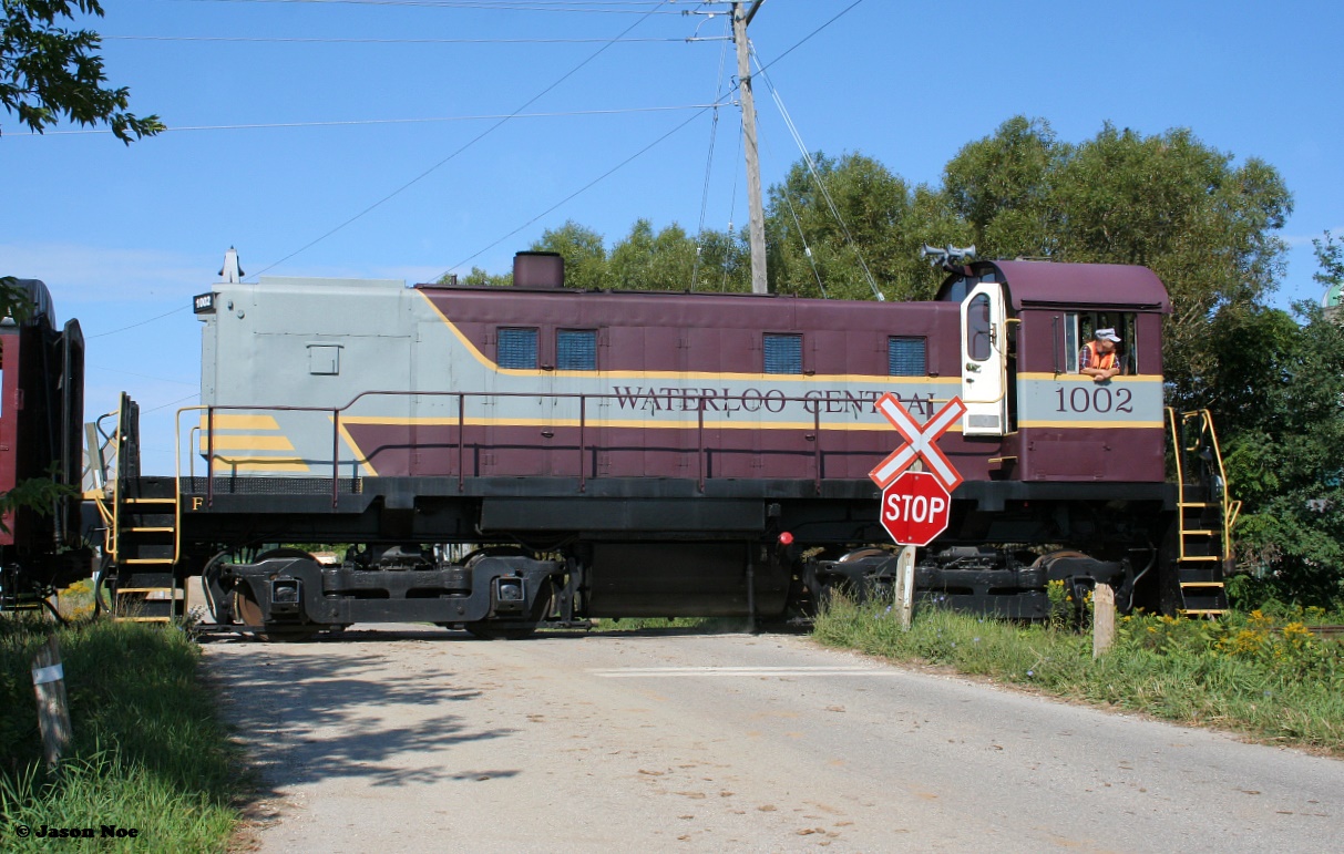 Following an extended hiatus due to the global pandemic, the first regular revenue Waterloo-Central Railway train to operate in over two years is viewed crossing Township Road 24 just north of the village of St. Jacobs, Ontario with S13 1002 leading towards Elmira.