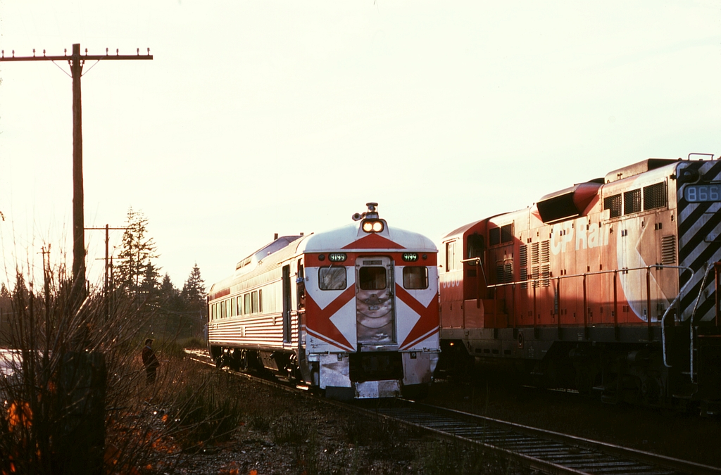 On Saturday 1974-12-14, E&N freight train No. 52 to Victoria with GP9s 8668 and 8819 and in-transit idling Baldwin 8004 was much later than usual, probably held for urgent traffic off the barge at Wellcox in Nanaimo, so headed in at the siding at Cobble Hill to clear RDC-1 9199 on passenger train No. 1 which appeared right on time at 0930 PST.  Working graveyard shift at Victoria roundhouse put me in prime position to know No. 52 was late, providing an excellent opportunity to catch the meet.

Note the rotating white beacon above the RDC’s headlight, part of a conspicuity test by the National Research Council, an alternate to the Gyralight usually carried below the window on the end door.  That test ended on CP 9199 on 1975-01-05.