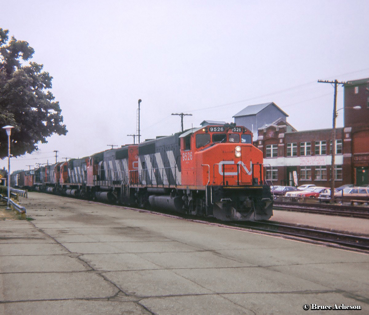 Westbound CN 431 rolls through Guelph station behind a pair of GMD GP40-2LWs, a pair of MLW bigs and another geep. Note the two vans on the head of the train, one each from PSC and Hawker-Siddeley.At right, Guelph's Granary Building is seen on Farquhar Street shortly before restoration. Built as a wood frame structure in 1858 by Toronto-based distiller Gooderham & Worts Limited, the granary was used for storing threshed grain prior to shipment over the Grand Trunk to Toronto. In 1914 the building was covered with bricks to extend the life of the structure, today holding the title of Guelph's oldest industrial building. Numerous industries used the site over the years, including locally-owned Saillian Rugs Limited, before it fell into disrepair during the 1980s-1990s. Restoration during the late 90s converted the structure into an office complex which today houses the Guelph Chamber of Commerce. This area once included Guelph's first railyard, which beginning circa 1900 included an interchange on Farquhar Street with the Guelph Radial Railway.