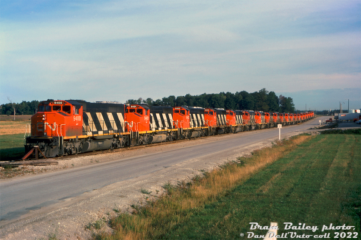 A dramatic downturn in traffic during 1975 resulted in some surplus CN power being parked. Here, a lineup of nearly new GMD GP40-2LW's sit in CN's MacMillan Yard with their radiator fans, exhaust stacks and horns covered over (similar scenes elsewhere on the system were likely). CN 9400-9419, 20 units in sequential order that had been built the previous year in 1974 (some still sporting relatively fresh paint), sit stored at the west side of CN's MacMillan Yard (south of the diesel shop, just north of the Langstaff entrance) await the eventual call back to duty.

CP, also affected at the time by the traffic downturn, used this opportunity to retire their FM/CLC fleet and return leasers.

Bram Bailey photo, Dan Dell'Unto collection slide.