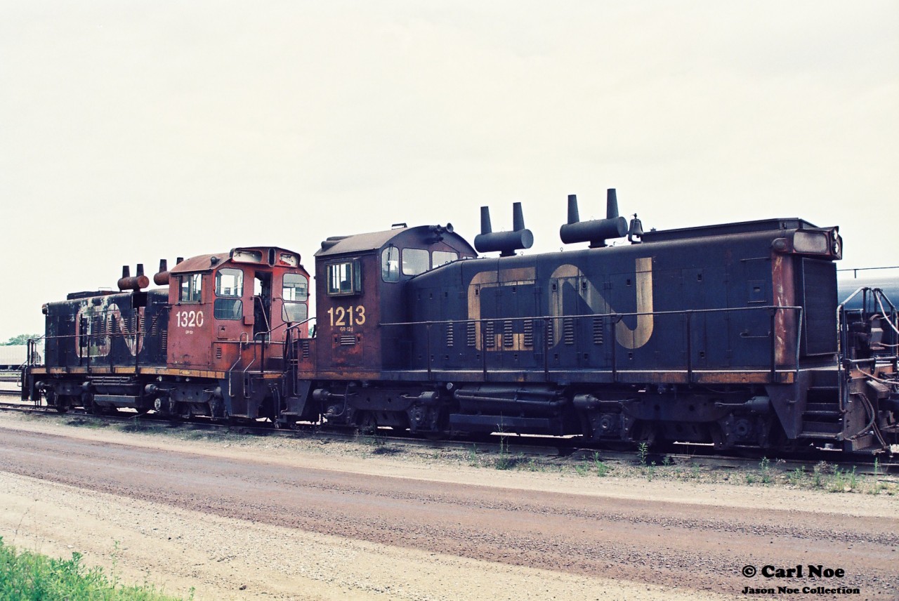 Two out of service SW1200RS’s are seen at CN’s Sarnia, Ontario yard during a hazy summer day. CN 1320 has signs of obvious frame damage.