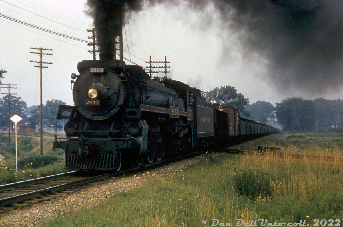 After waiting to cross just east of the diamond, Canadian Pacific H1a 2804 (a "standard" 4-6-4 Hudson built in 1929) displays an impressive amount of smoke she gets her 50-car freight underway out of London, heading eastbound on the Galt Sub crossing the diamond at Mile 111.7 with CN's Dundas Sub. The train is leaving the city from the east end of town, photographed from First Street crossing nearby.

Original photographer unknown (duplicate slide), Dan Dell'Unto collection slide.