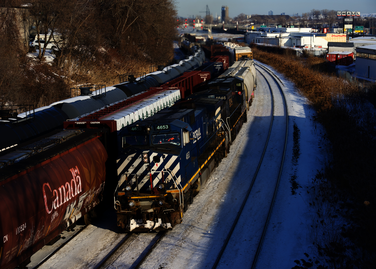 CN 321 is passing parked cars, including a classic cylindrical hopper as passes through Montreal West with a matched pair of BC Rail units.