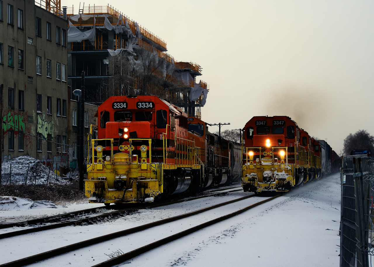 A pair of Quebec Gatineau northbounds both have clear signals ahead of them and are heading north on CP's Adirondack Sub. At left a grain train for Quebec City is slowly exiting the Côte-des-Neiges siding (with a pair of ex-BNSF SD70MACs trailing and 111 loads on the drawbar) while at right another Quebec Gatineau train is going faster, on its way to their yard in Sainte-Thérèse after interchanging with CP at St-Luc Yard.
