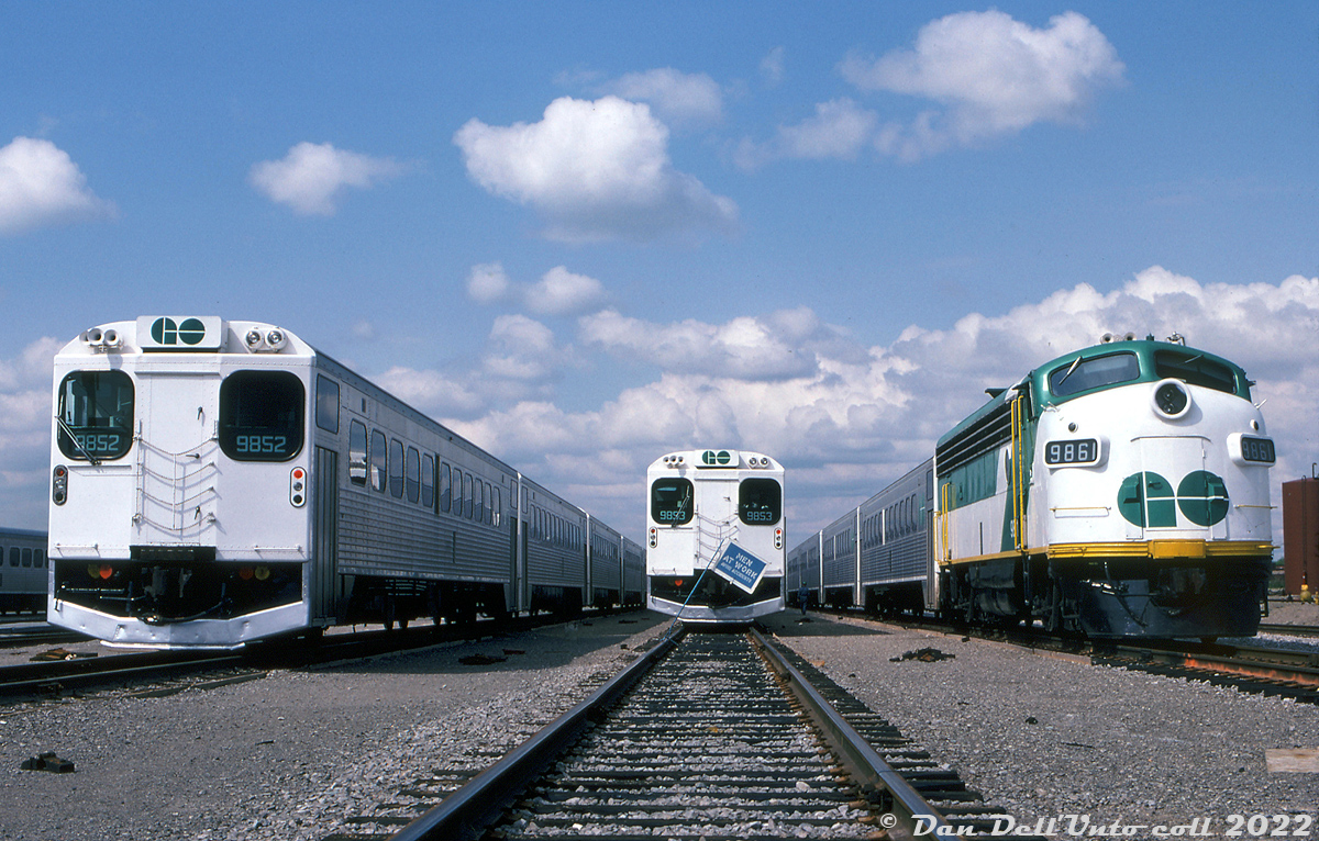 An almost picture perfect lineup: three GO Transit trains sit in Willowbrook Yard awaiting their next call to duty. Cab cars 9852 and 9853 mingle with APCU 9861 (still looking fresh a few months after entering service), all heading up consists of single-level Hawker Siddeley commuter cars. The flag clipped to the rail is "blue flag protection", noting to anyone around that crews are working on that consist in the yard.

Original photographer unknown, Dan Dell'Unto collection slide.