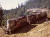 On Vancouver Island, CP’s line from Parksville to Port Alberni was ruled from 1949 to 1971 by Baldwin diesels, but increasing tonnages from the mills in Port Alberni plus the risk of fire from the common steel brake shoes on prolonged grades resulted in trial of pairs of GP9s with dynamic braking.  At the same time, due to advanced age of two large timber trestles, diversions on culverted fills were constructed.  This is an eastward train powered by 8684 and 8649 on the Four Mile Creek bridge at mileage 24.4, just east of the siding at Stokes.  In another half mile, bridge 23.9 over Five Mile Creek will be encountered.

<p>Stokes, in common with numerous other stations on the Port Alberni sub., is named for one of its surveyors, this one for William Marpole Stokes, later an E&N division engineer.