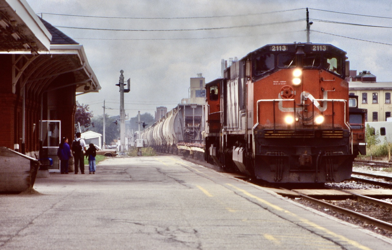 This was an early on slide for me, and still one of my favourites. This was my first visit to Kitchener station, and at the time I knew all the 251 powered Alco/MLW’s were on borrowed time. All the six axle vets were already gone but the slightly newer Bombardier built HR616 would last a few years longer than the other six axle non cowl versions. High reliability was certainly not something these units lived up to and spent almost as much time out of service, as they did in service. While the motive power this day definitely caught my eye, so did the kids taking in the action that definitely helped make the photo. Over the years I have spent a lot of time at the old station, day and night. Fond memories for sure. Here train 432 prepares to stop and work the yard, with a crew member dead heading in the trailing M420, and a long cut of salt hoppers out of Goderich trailing the power and flat cars.