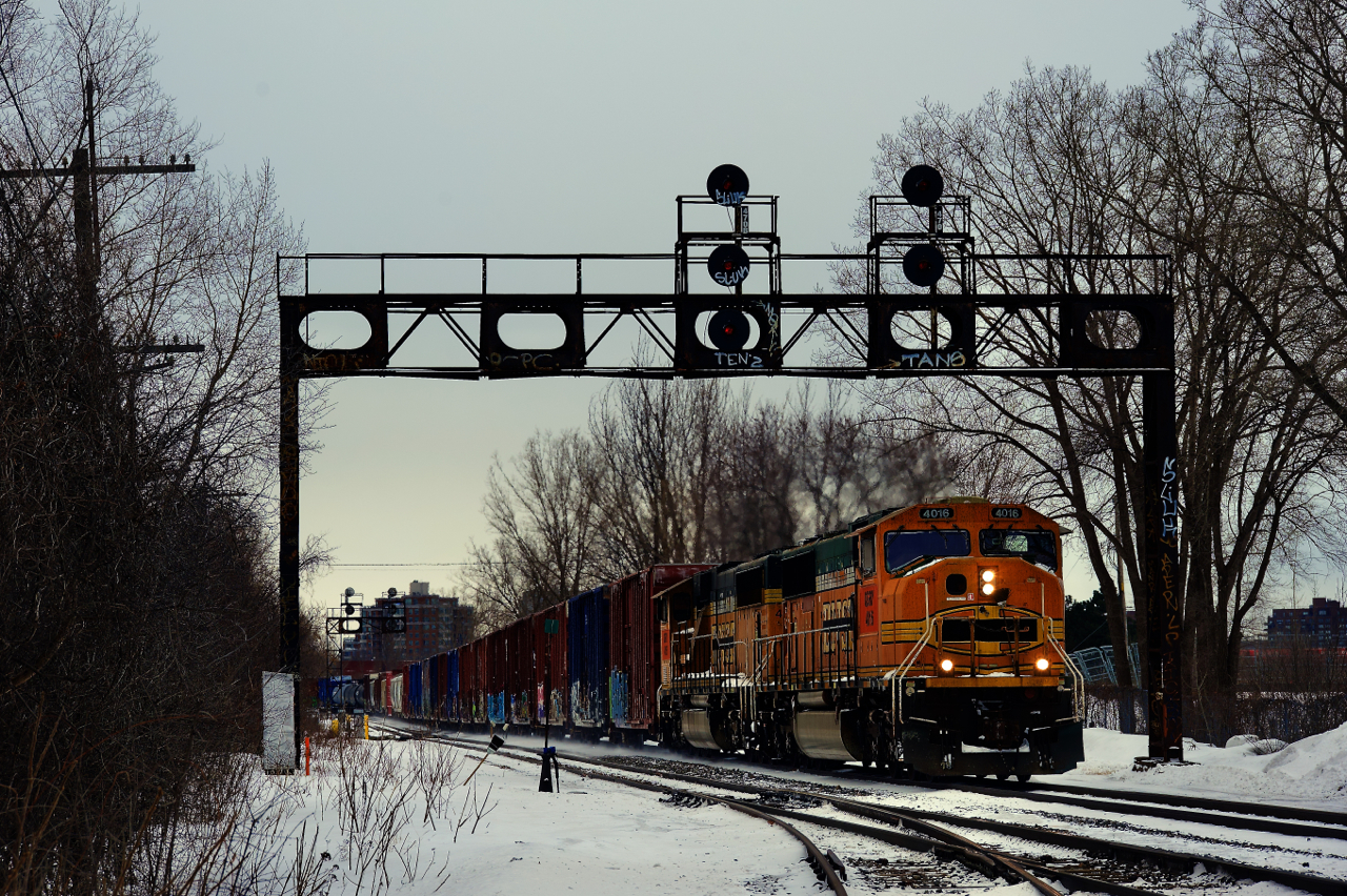 A pair of ex-BNSF SD70MACs with consecutive numbers (QGRY 4016 & QGRY 4015) is leading their train under a vintage signal bridge as they leave CP's St-Luc Yard.