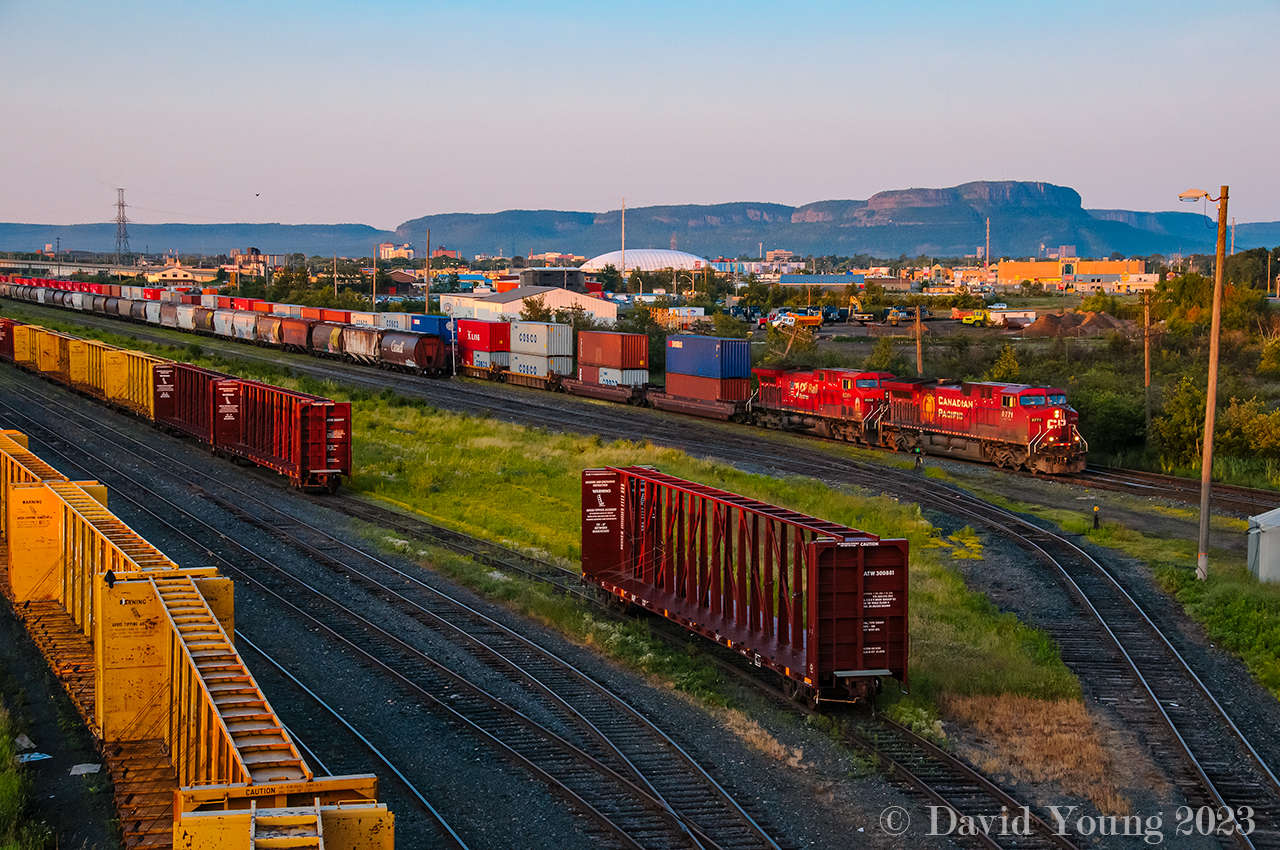 Sunrise in the Intercity. Stored centrebeams in CN's side of "D Yard", while a string of grain loads are observed in CP's portion of "D Yard", blocking the view of Vancouver to Toronto train 110-17, who is moments away from pounding the diamond with CN's Kashabowie Sub in Thunder Bay's Intercity with CP 9771-9564 leading.