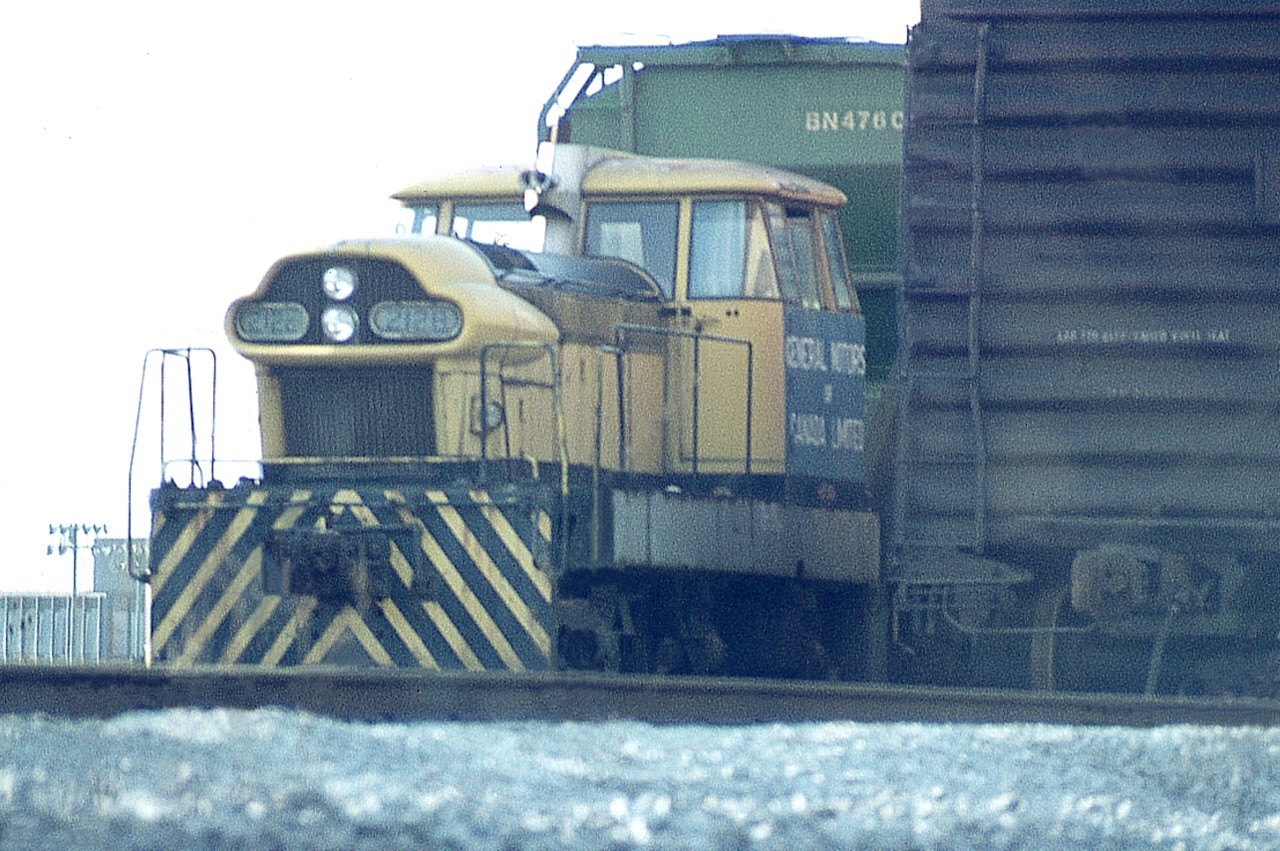 I cannot recall how many times I slithered into the GM Glendale Av plant property trying to get a shot of this unit. More times than I can count.  Finally; got this one so-so image thru a fence, and I never saw the unit again.
This is GMDH3 #2128, built in January of 1960, a demonstrator. It even went overseas to get attention but never did drum up any sales. It was on trial as #275 in various localities until September of 1963 it went to McKinnon Industries, which later became General Motors plant that we know down by the Welland Canal. In 1992 it was sold to South Simcoe Railway up in Tottenham. It again wore #275 and was now painted a dull black.  Then became surplus, and in my mind it was foolish to let it go. The unit now calls home at South Michigan Railroad Society, out of Clinton, Michigan.
For some strange reason I have not been able to find any photos of it wearing its GM colours at the plant. Odd, because it was there nearly 30 years. Before and after photos are out there though.  One of a kind. Maybe someone can steer me to where there are examples on the internet.