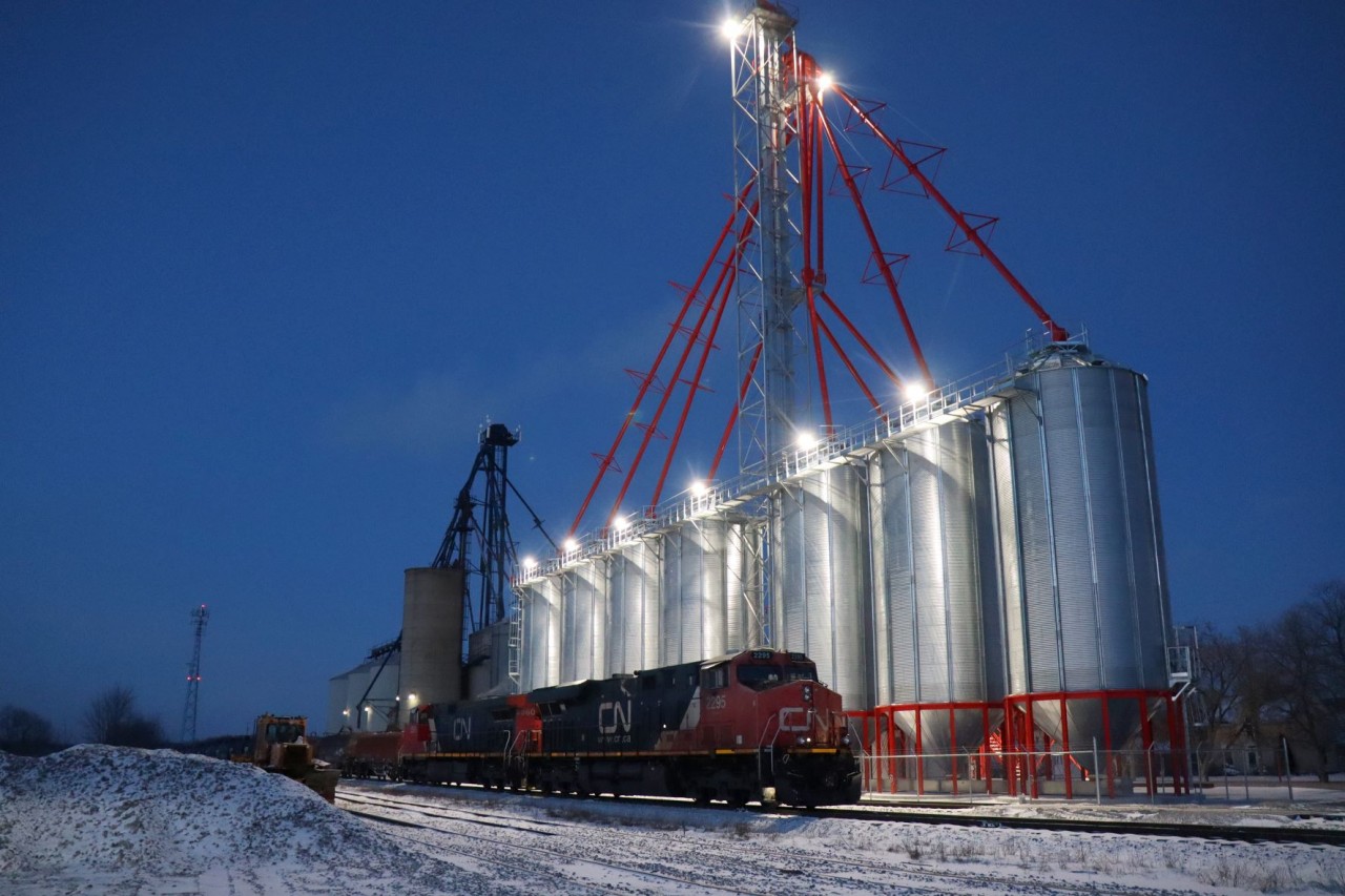 Just driving by Railview Transload Elevators, this March evening on the way home, and to my surprise an extremely late CN 502 was clearly visible idling on the main.  The crew had obviously run out of hours and conveniently parked their train under the bright lights of the new, Mustard Silos.  A rare photo opportunity indeed and one not to be missed.  I had sufficient time to capture this setting from both sides of the power CN 2295 and CN 2560 before the new crew arrived to continue south to Garnet Yard.  
I believe this capture qualifies for the Time Machine in conjunction with John Eull’s 1986 photo (Photo ID: 4356) and my existing companion photo of 2011 (Photo Id: 24926). These three photos present CP, SOR and CN powered trains at the same location albeit hauling different freight and depicting expanded facilities/service, etc.