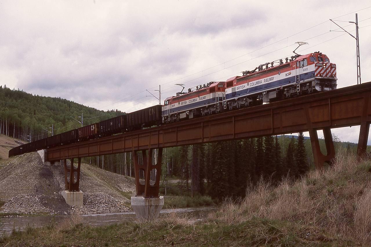 Heading for loading at the Quintette mine, BCOL GF6C electrics 6005 and 6003 are eastbound with coal empties under the 50 KV catenary and crossing the bridge over Bullmoose Creek.