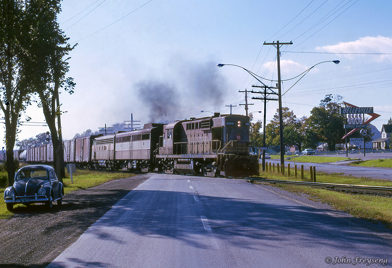 Shortly after an eastbound led by a pair of RS10s departed Belleville, another eastbound behind RS10 8469, FB-1 4409, and leased Bessemer & Lake Erie F7A 718 throttles up crossing Highway 2.  My 1958 VW Beetle off to the left.Scan and editing by Jacob Patterson.
