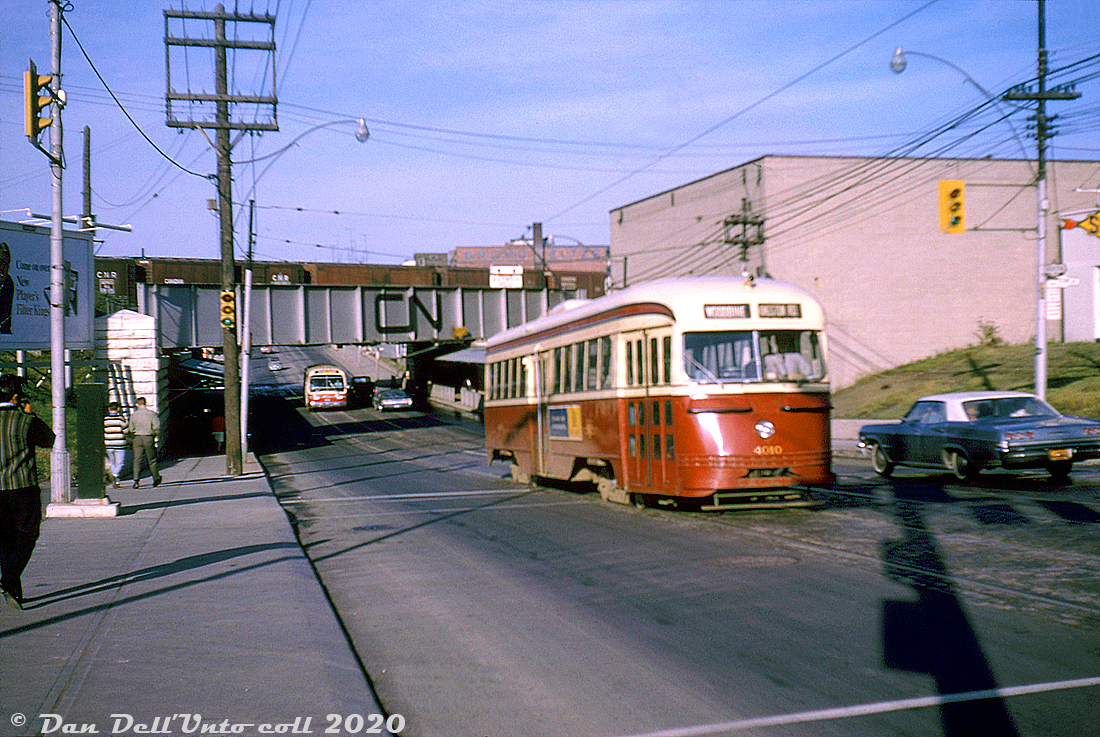 TTC PCC 4010 (A1-class, part of the first order of PCC's built new for Toronto by CC&F in 1938) heads eastbound on Queen Street West at Gladstone Avenue on the Kingston Road route, passing through the Parkdale area of Toronto and climbing out of the dip under the CN Weston Sub and CP Galt Sub railway underpasses (the "Queen Street Subway", built in 1897). Some CN 40' boxcars occupy the closest bridge span, which is painted fresh silver with the then-new CN "noodle" logo in black. A TTC GM New Look bus follows behind the streetcar, possibly a Dufferin bus lining up for turning north onto Gladstone (navigating the "Dufferin Jog" traffic had to make around the railway underpasses.

Original photographer unknown, Dan Dell'Unto collection slide.

Note: This slide is a little soft on the right side. Apparently in the 1960's there was an unknown US-based transit photographer (possibly a fellow named John H. Eagle) who took many photos on his US and Canadian travels with a slightly misaligned lens, that always showed on the right side in his slides (making them easy to identify). By the 70's it appears the unknown photographer had it fixed or upgraded to a better camera.