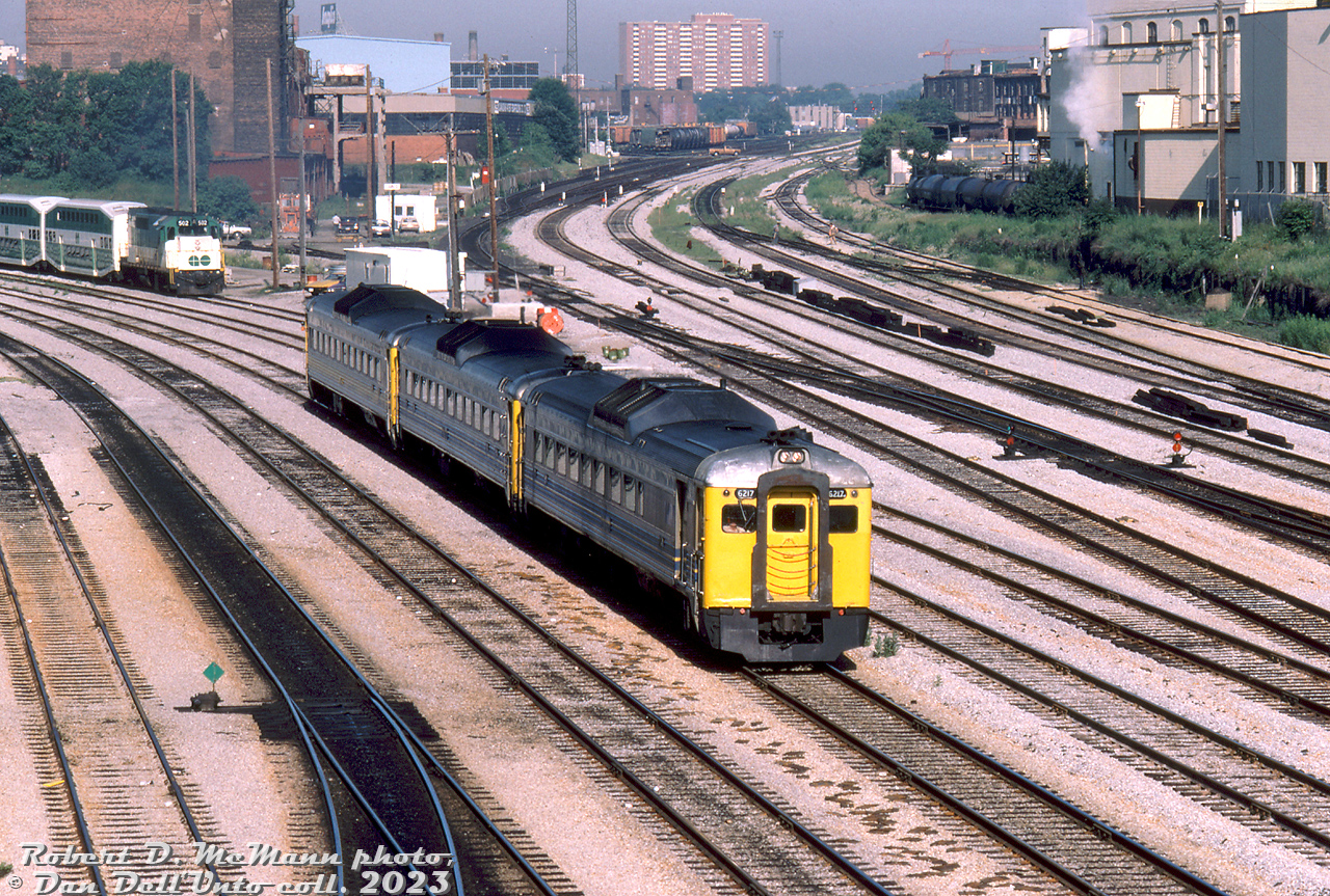 A three car train of Budd RDCs lead by VIA RDC-2 6217 (ex-CP 9115, still in service today with VIA) comes off the Oakville Sub at Bathurst Street, heading inbound into downtown Toronto nearing their destination of Union Station. A GO train with GP40TC 502 appears to be waiting to depart TTR territory and head westbound on CN's Oakville Sub (possibly a morning train deadheading back to Willowbrook). CN's Weston Sub can be seen heading off into the distance, with CP's Parkdale Yard (then on borrowed time as a freight yard) beyond Strachan Avenue grade crossing. On the right tank cars are spotted by the old Toronto Municipal Abattoir that operated off of Niagara Street.

Robert D. McMann photo, Dan Dell'Unto collection slide
