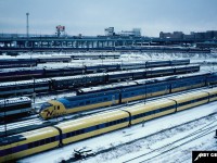 On a winter day, VIA Rail (formerly CN’s) Spadina coachyard in downtown Toronto, Ontario is viewed in winter 1982. All the tracks are packed with passenger equipment, including an Ontario Northland TEE train for the Northlander and VIA Rail cars from the blue and yellow fleet and old heavyweights including some cars still painted in their former CN colors.