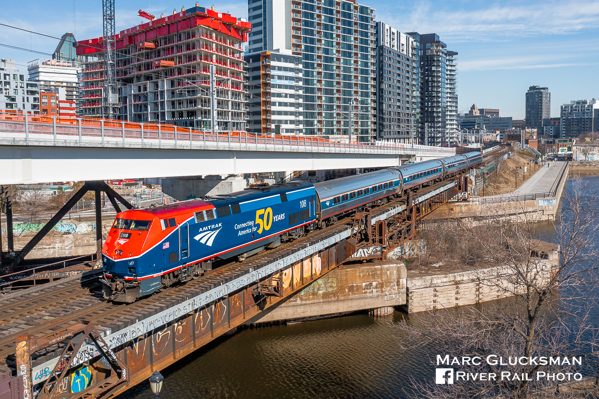 Peel Basin Looks Different. On April 4, 2023, Amtrak Train 68/Canadian National Railway Company 694 (Adirondack) was getting ready for its first departure from Gare Central in Montreal, QC with revenue passengers in over 3 years, this day with AMTK 108 (50th Anniversary/PhaseVI, P42SC) leading. The scene at Peel Basin near the St. Lawrence River in Montreal has changed dramatically in recent years, as the super structures on the bridge have been removed, a light rail line right of way is being put in place, and significant amounts of residential housing is under construction.