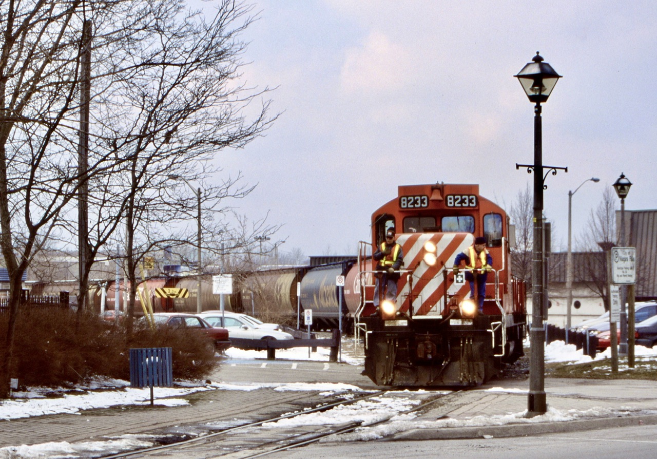 Niagara Falls is one of those cities I wish I had explored a bit more back in the 90’s and early 2000’s. Back when CP and CN had more of a presence in town. It is amazing how many industries once called Niagara Falls home. The CP transfer job to CN allowed some interesting shots though the middle of old downtown as well as rolling through a residential area. I was lucky enough to catch this job a few times, like this day. Here the job was returning from CN with a good cut of Canadian grain hoppers as the train spits the public parking lot at Erie Ave and Queen Street. The crew are on the front porch keeping an eye out for motorists. Today sadly all the rails are long gone here.