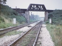 It has been at least 8 years since on this site there was a discussion about the CN Thorold Sub north track bridge over the CN Grimsby sub down by the canal at Merritton. Knew I had a photo somewhere. Finally found it.
The Thorold Sub used to be a two track main, and pictured is the north track bridge as it went over above the Grimsby and down into the yard at Merritton.  The bridge was removed in 1976 although some of the track on the north side leading up is still there. The Thorold sub used to be  busy line until the Canal Bypass was built in 1968-70 and what used to be the Welland sub became the Stamford and a connection was put in at CN Clifton, bypassing the steep grades at Thorold.
I had been told that this bridge was known locally as "Bum Bridge" as it was a hangout for hoboes and others hopping trains and was the source of many injuries due to reckless behaviour of those who frequented the area.  So the bridge is long gone but part of the abutments can still be seen.  In this image looking west the background visible is the Merritt St overpass and behind that, the old Merritton NS&T bridge.
Note in the foreground the canal 'derails'.