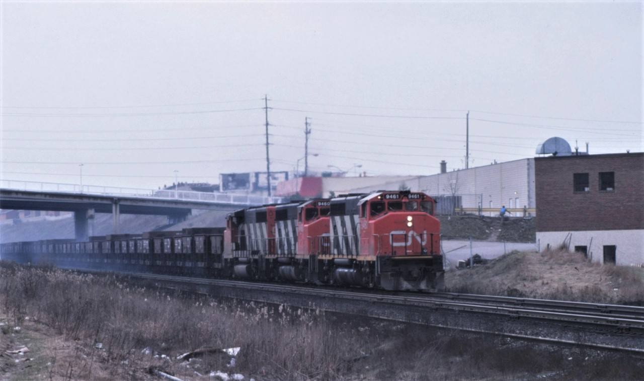 On a crappy smoggy spring day in Toronto, a drag of ore cars drifts downgrade on CN's York Sub and under the Yonge Street bridge.  Brake shoe smoke is quite evident as the train slows for the 15 mph turnouts and curve at Doncaster as it will head north on the Bala Sub to Sudbury for more slag.  Power for the train was a matched set of GP40-2(W)s 9461, 9460, and an unknown third 9400.