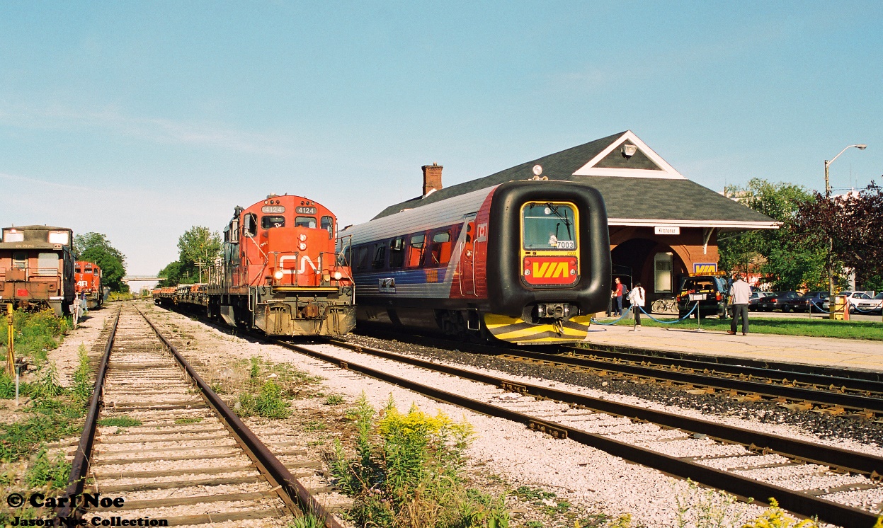In September 1996, VIA Rail had launched the testing of two IC3 Flexliner demonstrator sets on some of their routes throughout Ontario. These new units were designed and built by ADtranz, which was a new company spin-off created from ABB and Daimler-Benz. These two trainsets entered revenue service on September 29, as it was concurrent with the release of the new VIA Rail system timetable that touted the trains as a “commuter service.” 

VIA Rail officials had rolled-out the blue carpets for an official unveiling at the Kitchener station during a weekday afternoon. This trainset was on display for several hours before heading west to Stratford later in the evening on the Guelph Subdivision. However, while everyone in attendance enjoyed the festivities, the daily regular work would continue as here the CN 15:30 Job with CN GP9RM 4124 and it’s train of empty flatcars is pictured slowly passing the event as heads for the Huron Park Spur and the Budd Plant. In the background are caboose 79713 and CN 4138.