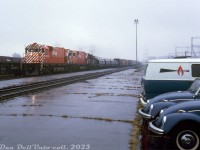 The action red paint on brand new CP Rail M630 units 4570 and 4571 cuts through the gloom as they pass by the platforms of Leaside Station on a westbound extra freight (white class lights and flags present) with an 8400-series RS3 trailing. Not sure what was up with the matching VW bugs, perhaps some railfans out for new power, or maybe they belonged to a local company that used the parking lot.<br><br>Due to teething problems with their 65 5500-series GMD SD40 units, CP turned to MLW for the 3000 horsepower 6-axle M630 model to operate their new Locotrol (distributed power) coal trains out west. CP 4570 and 4571 were two of the 29 units purchased by CP in 1969-1970, outshopped from MLW's Montreal plant and added to the CP roster on October 17th and October 20th 1969, respectively. They were assigned to Alyth for maintenance purposes and had to get out west to their coal-hauling duties somehow, so they were worked west in general freight service, as seen here!<br><br>Eventual reliability issues resulted in the big M's coal tenure lasting only a few years, and the fleet was moved east to run out of the MLW hub of St. Luc when enough brand new (and improved) GMD SD40-2 models displaced them in coal service in the mid-70's.<br><br><i>Original photographer unknown, Dan Dell'Unto collection slide.</i>