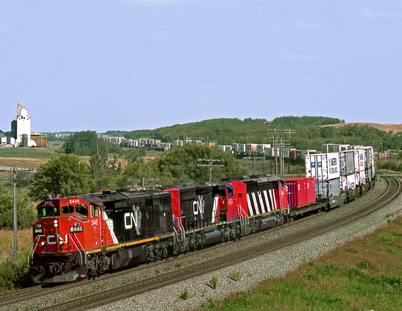 Westbound containers curve through the Arrow River Valley in western Manitoba. The abandoned CPR Miniota branch ran parallel to the CN through here and the elevator is on the CPR RofW alignment.