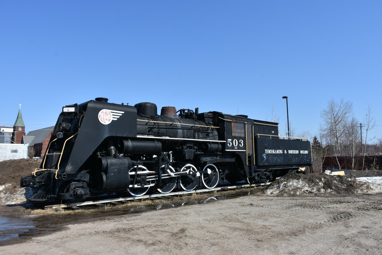 2-8-0 T&NO 503 sits on a track panel at the end of a public parking lot just south of the former Canadian Pacific station (now North Bay Museum) on this nice, warm, cloudless, sunny April afternoon. There's a little graffiti on the tender, but the real damage is in the now sealed with steel plating cab area. I understand there was some arson vandalism a number of weeks ago prompting the new protection on the cab window and door openings. 
503 sits just a few meters from the fenced compound that houses the last two remaining pieces of ONR Tee-Train equipment. 
http://www.railpictures.ca/?attachment_id=51749