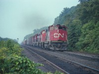 Moving sharply down that long nine mile grade that stretches from Copetown to Bayview, an eastbound freight with two MLW M-420s on the lead is approaching the site of the old Dundas station at mile 4.7 or so. It is approximately 0900 and the sun is not yet up and penetrating the morning mist. Power on the train is CN 2545, 2543, 9454 and 9416. In about 3 years the M-420 series would be renumbered into the 3500s.