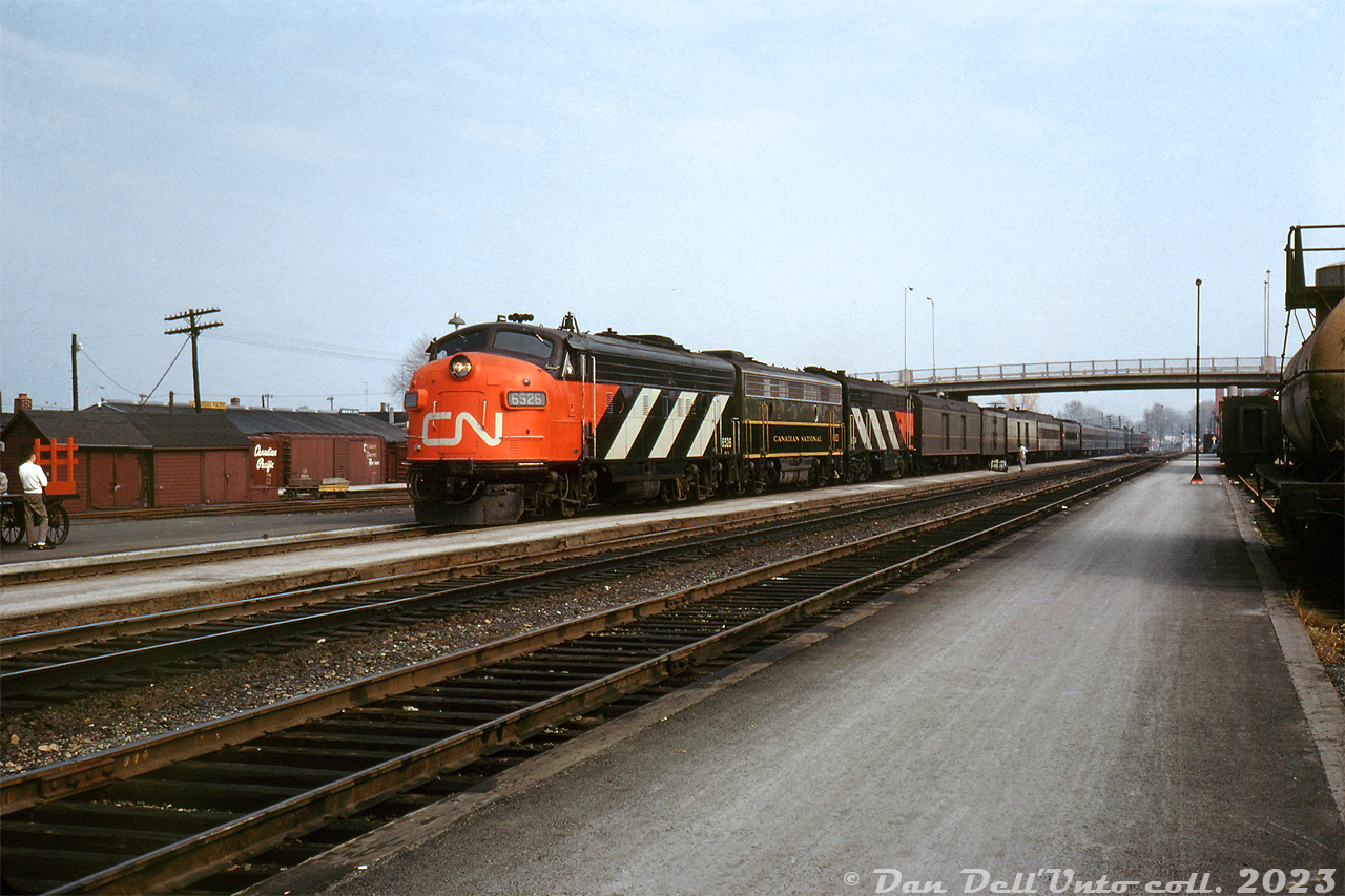 The new image of CN: GMD FP9 6525 and CLC CPA16-5 6704, both in fresh zebra stripes and sporting the new CN "noodle" logo, bracket F9B 6621 in the older green, black and yellow livery as they pull into the station at Brockville with a westbound passenger train. The new modern logo and livery (first unveiled in 1961) was still in its infancy at the time of this photo, evident by the passenger and head-end baggage and express cars all still sporting the older paint scheme (if one looks closely, there appears to be a maroon private car on the tail end).

In the background are the nearby CP freight sheds, with 40' boxcars spotted at the loading platforms.

Original photographer unknown (slide labeled "Stewart" on the back), Dan Dell'Unto collection slide.