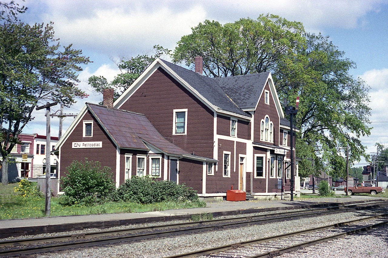 About time I posted another railroad station shot.    I've always loved this particular place.  Classic old style, all wood and living quarters built in. Note the red saltbox out front. Don't know when this station was built, (oldest photo I have seen dates 1905)  but the Petitcodiac and Elgin Branch Railroad Company was the first thru here in 1876; a northward line off to Havelock was laid in 1885 but good money was never really made. It was pulled up in 1993 and the Intercolonial took over the main line in 1919. 
When this photo was taken, the station was served by two RDC powered trains each way daily. By the mid-80s it was just the one, with the  VIA 'Atlantic', while seen, did not stop.
With the so-called 'progress' on the railroad scene, the building was considered redundant and torn down in the late 1980s. I haven't the actual year, and am curious.
It is a shame this village has lost a landmark.