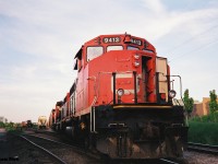 On a summer evening in 1993, CN 413 with lead unit 9413 west, was sent down the Guelph Subdivision to Sarnia, Ontario. Train 413 was a very high priority finished vehicle train that had operated between Oshawa and Sarnia where the auto racks made their connection to the US. On this evening, the train had to take the siding at Kitchener to meet the joint VIA Rail/ Amtrak International before proceeding west. Here, with the crew at the popular Dairy Queen, CN 9413 is viewed at the Kitchener yard near Lancaster Street. 