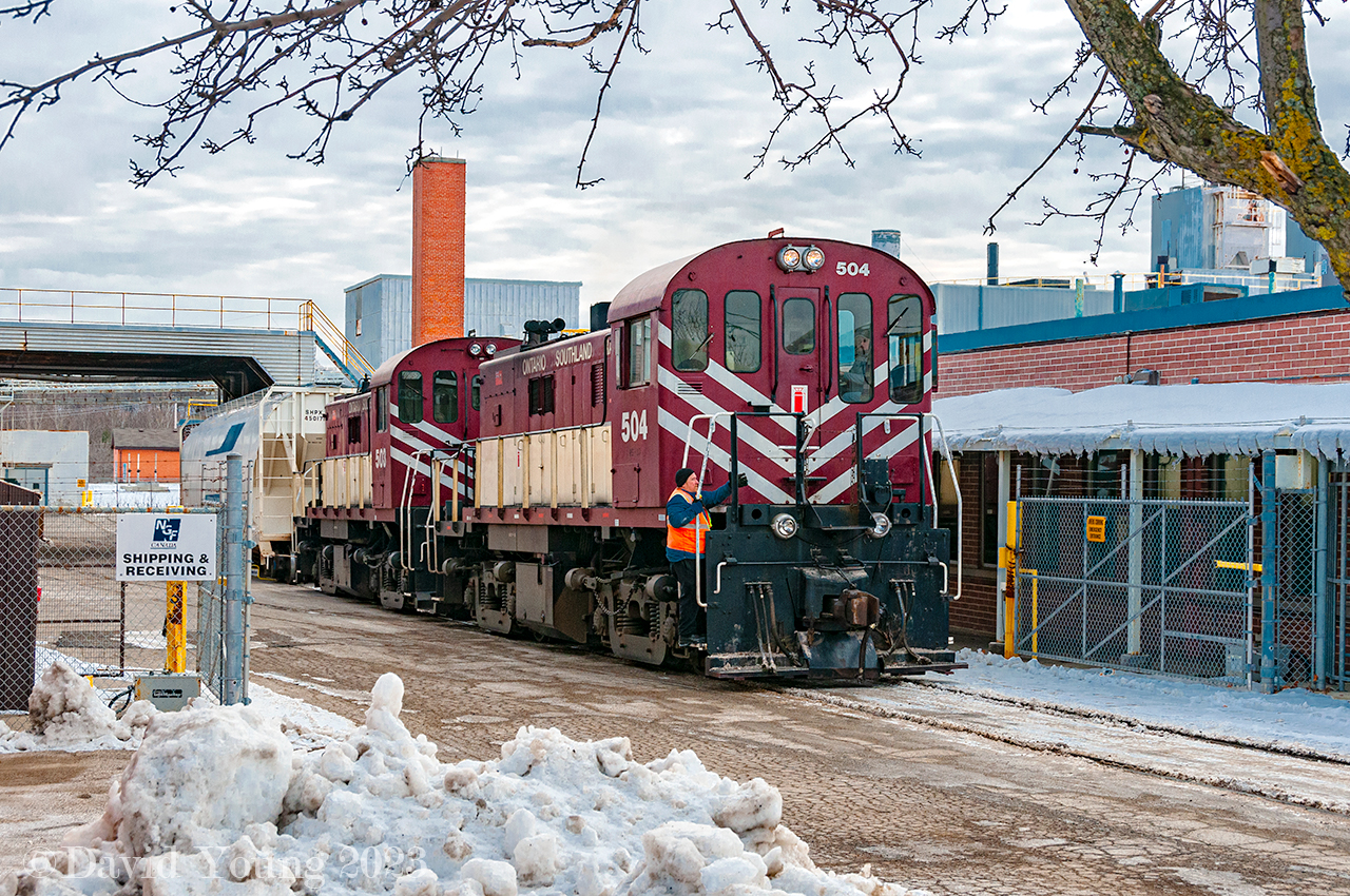 Having completed their switch at Owens Corning Fibreglass, Ontario Southland Conductor Mercer rides the footstep in anticipation of his next task, flagging vehicular traffic approaching the crossing on York Road. Those ACFX hoppers looked so clean in the first decade of the 21st Century. Compare it to this shot by  Mr. Host over a decade later, they have really got their "tan" on.