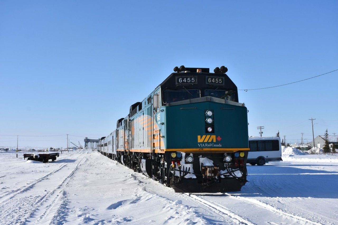 Since it's starting to get a little warm outside (at least in the Hamilton/Niagara region) I thought I'd offer up a little cold and snow photo to remember the winter we just left behind. 
Empty flatcar, empty yard, empty grain elevator, empty passenger train! 
Arriving as VIA 693 'The Hudson Bay' earlier in the day at 09:00, the consist sits idling in front of the Churchill, MB station. All passengers have detrained, and the last few shuttle vehicles remain gather on the platform to collect the last baggage for delivery to various lodging locations around the town. 
In a few short hours at 19:30, this consist will become VIA 690 and will begin its southward journey to The Pas, MB. 
In the meantime, I have 9+ hours to walk around the town and railyard looking for some interesting images to capture.