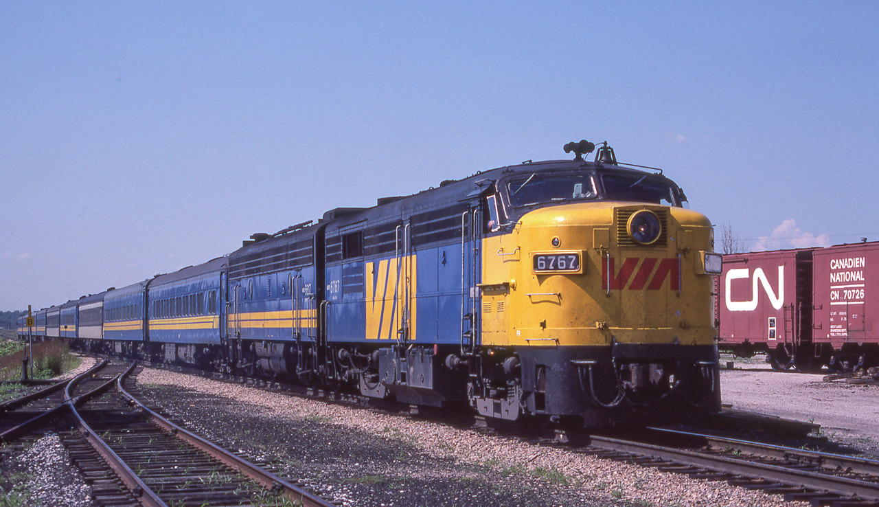 VIA 6767 is eastbound in Komoka, Ontario on August 13, 1982.