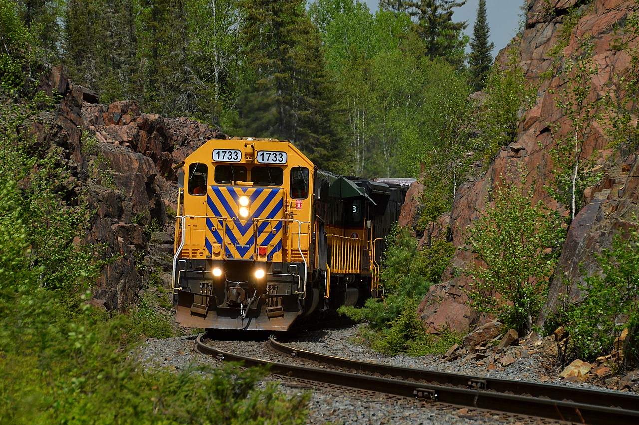 Boston Creek. Nice rock cut. I just did not feel like climbing up onto the cut as I have done it a few times before and was not in the mood to take a chance on tripping or falling as it is getting rather overgrown in there now. So this shot is of the Noranda train returning south, and taken from near the roadway crossing.
ONR 1733, 1730 and 2123 is the power. Now normally #512 returns from Rouyn-Noranda after dark. It was so flamin' hot up there that sun kinks developed along the line east of Kirkland Lake and the train was left at Northland Park on a siding until next morning.
After the line was inspected and the #213 (Englehart to Cochrane)) had cleared the junction at Swastika, then the #512 would be ready to come down.  So it gave us time to scurry over to the cut at Boston Creek.
Those who have been in this area know this road is rough. It is pegged at 80 KMH and for fun I tried to find a spot where I could actually get up to the posted speed limit without rattling every bolt out of this poor vehicle. More like 40 KMH is what we did most of the way, 6 KM drive off of Hwy 112.
The 2123 is a newby to the ONR, purchased last year and was formerly NS 2639. It is one of five SD70Ms purchased. One other, 2121, is painted up ONR colours and looks great.
