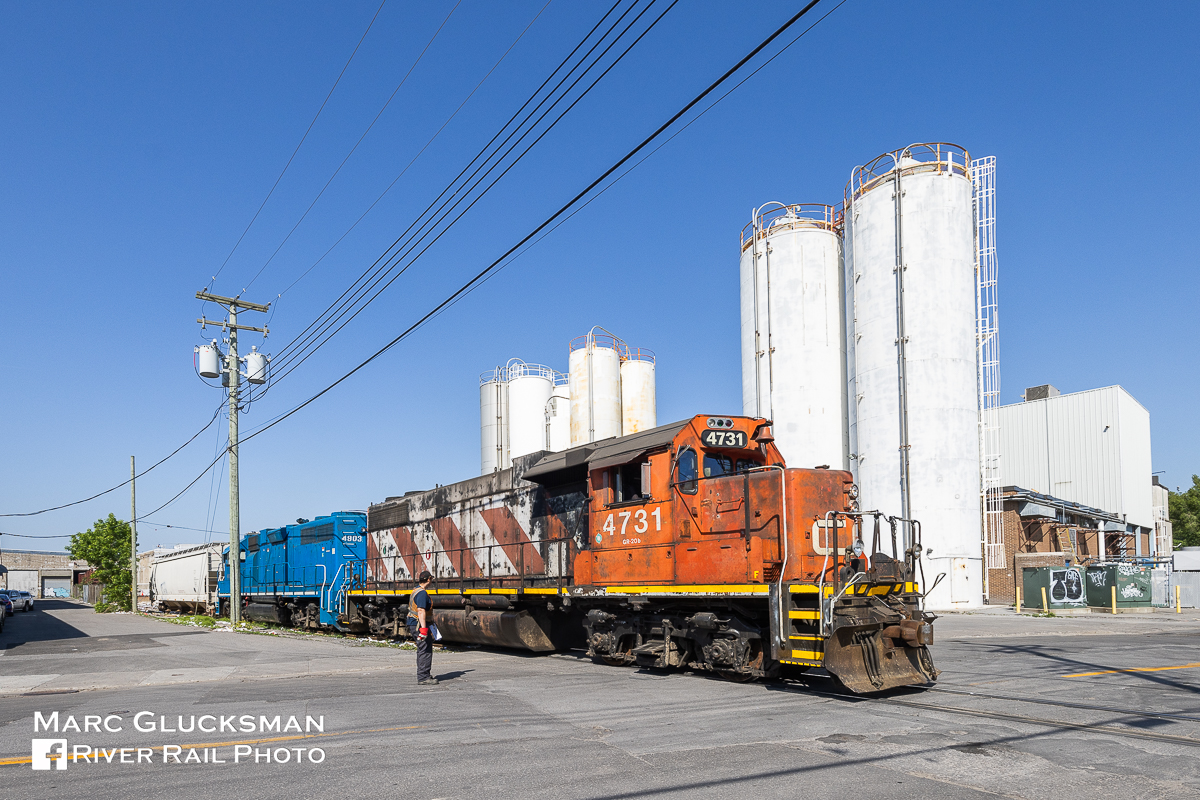 Urban Packing. On the morning of Monday, May 30, 2023, the Pointe-St-Charles switcher/Canadian National Railway Company 500 with CN 4731 (née-CN 5531, EMD, GP38-2/GR-20b, 4/1973) and CN 4903 (ex-GATX 2255, née-GTW 5809, EMD, GP38-2, 11/1971) are seen retrieving a covered hopper on the Turcot Holding Spur, South East, Montreal, Quebec, after dropping off 4 box cars for Kruger Packaging. This job travels bi-weekly out of the yard and down this short line, on this day utilizing these veteran EMDs. The conductor is talking to the engineer at Place Turcot just before the train returns to Pointe-St-Charles Yard.