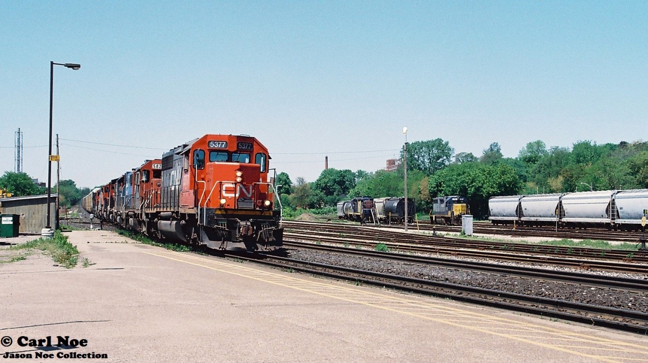 During a spring afternoon, CN 384 with 5377, GT 5822, GT 5859, 9624, 5763, 2425, 2547, 6015 and 5022 is passing the Brantford, Ontario station on the Dundas Subdivision. Also, HLCX 113 and RaiLink 1751 were the Southern Ontario RaiLink power in the yard in Brantford on this day.