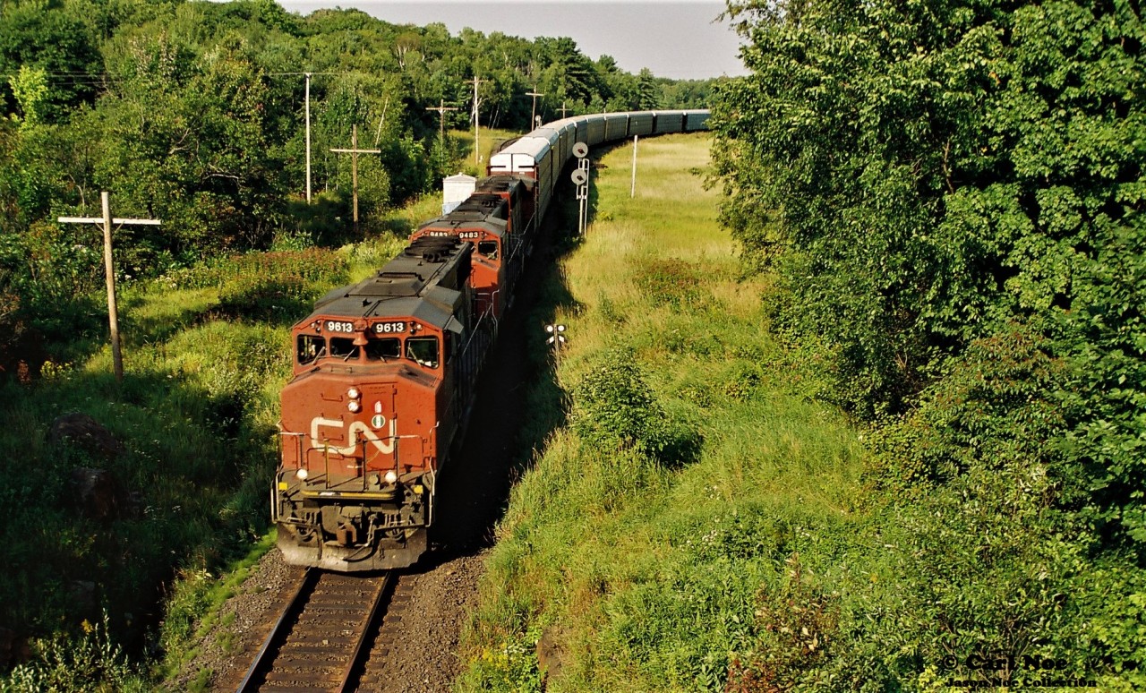 During an August evening a CN northbound is viewed about to duck under the bridge at Falding, Ontario on the Bala Subdivision with 9613, 9483 and 9460.