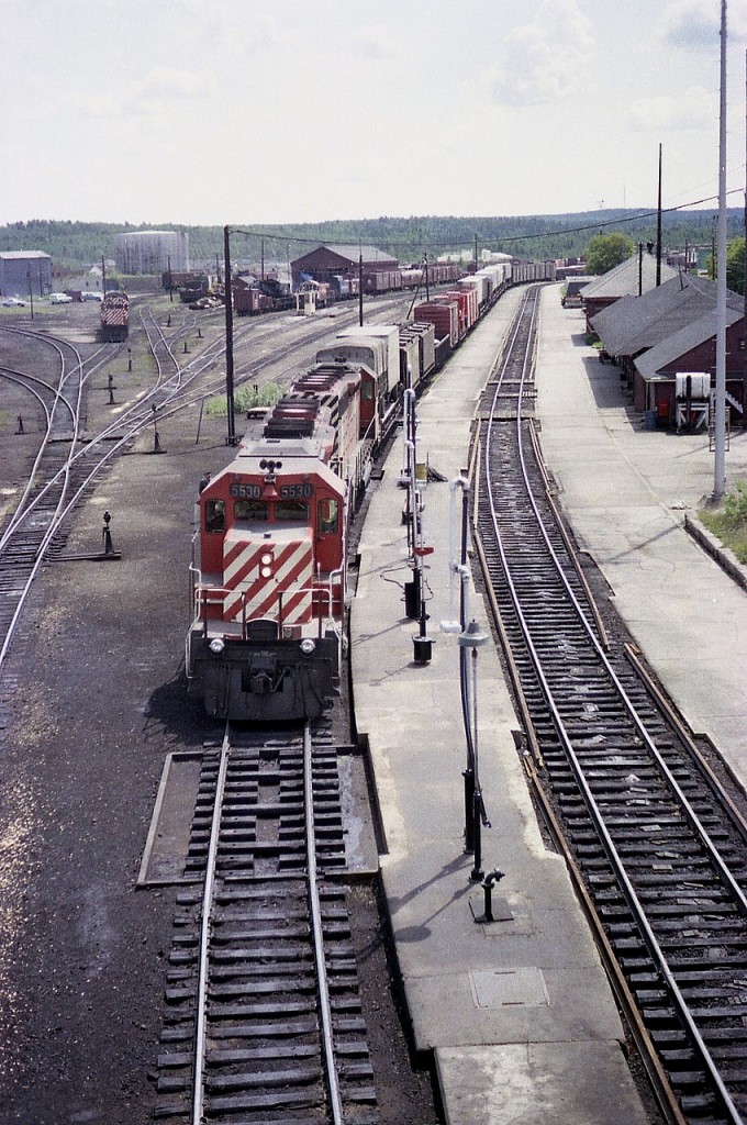 Decent view of the old yard at Chapleau from 1977 showing various MoW equipment and rolling stock as well as a couple of locos. On the right is a freight building, a former station and a new modern station (flat roof) in behind.  Westbound CP 5530 and 5542 about to leave the Nemegos Sub for the White River sub after a crew change.
Photo taken from overhead walk bridge.