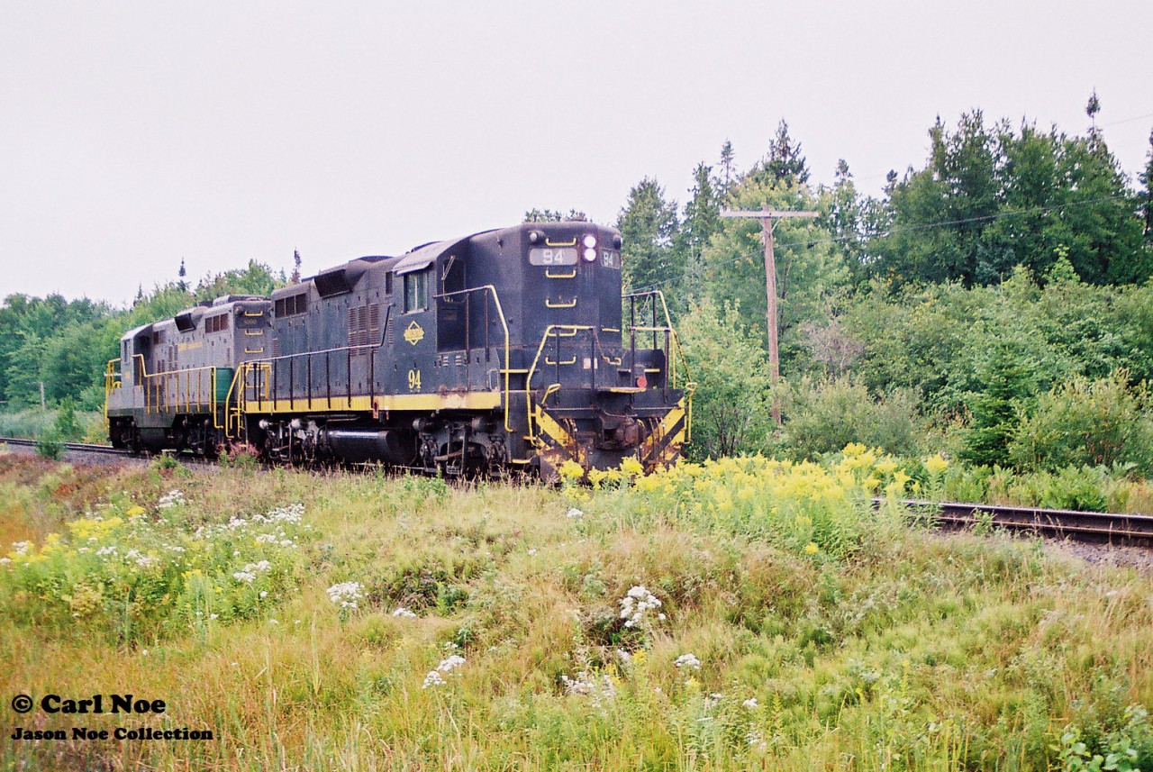 n  In 1996, CN had officially abandoned their Newmarket Subdivision between Barrie and Longford Mills, severing the mainline as a through route and putting the Canadian on the preferred Bala Subdivision route permanently. While this section of the line had received extensive attention during its final runs, CN had also deemed the northern section of its Newmarket Subdivision between North Bay and Capreol as no longer required as the only freight traffic on this portion would have been occasional run through trains using the subdivision to reach Capreol. And with trains 450/451 only operating between Toronto and North Bay it was put up for discontinuance. Following its approval of abandonment, CN had contracted emerging company Cando Contracting to remove the heavy mainline rail for them. In the days before internet, cell phones and social media this lengthy operation basically went on virtually undetected and photos are very scarce despite the fact this was still an active mainline until the end. A lot of this had likely to do with the majority of this line being very remote and photo locations not very accessible.
So then this is where the expect the unexpected part of the hobby comes into play during one of yearly northern Ontario railfan trips.
In late summer 1997, a group of us were heading to Sudbury and decided to detour through North Bay during the morning, hoping to catch something on the Ottawa Valley Railway along the way. That morning, it was very foggy and after some photos at the CP North Bay station we continued our journey on the Trans-Canada Highway towards Sudbury. I believe some of us were even beginning to start nodding-off when a friend suddenly said “Ah buddy there’s GP9’s over there!” Yup there sure was. Catching us totally off guard were Cando Contracting 1000 and 94 as they slowly appeared between trees , headed to their waiting rail train that was likely situated somewhere in the remote wilderness. At this point the line started paralleling the highway from North Bay within sight so we were able to get ahead of the units and quickly pulled over at the crossing where the Trans-Canada highway intersected it. A mad scramble ensued as camera bags were quickly opened and we all piled out of my dad’s van as we set-up to photographs the units going over the highway. The crossing protection had been previously disconnected so Cando workers had to protect the movement each time a train crossed