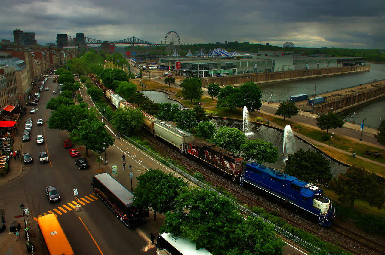 As seen from a tower that is part of the Pointe-à-Callière Museum, CN 500 is seen leaving the port as light rain falls. CN 4903 & CN 4731 is the power on this 12-car train.