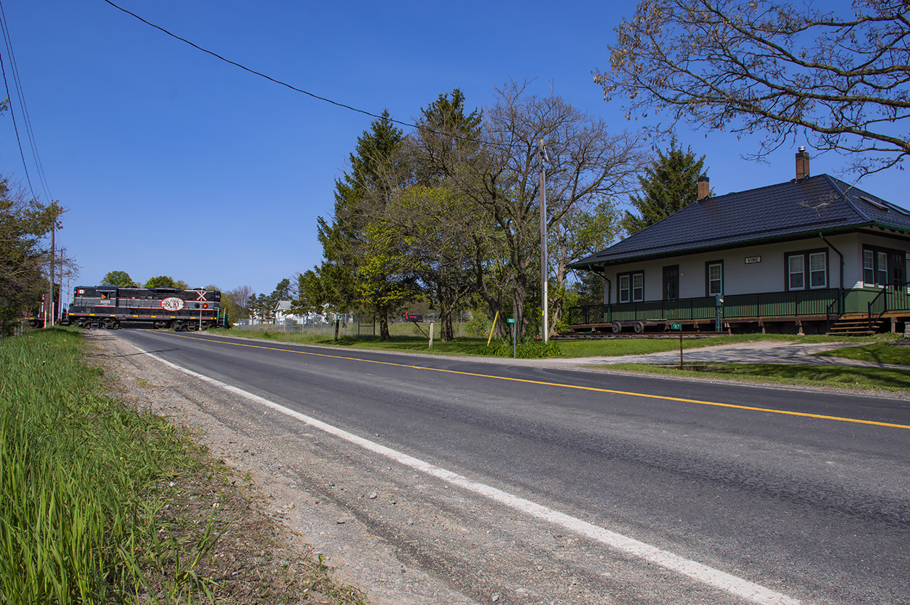 The old Hamilton & North Western Railway line through Vine, Ontario still sees a train pass by twice per week as the Barrie Collingwood Railway’s GP9 1001 works down the Beeton Sub to industries at Innisfil and back through Barrie to Utopia.  The circa 1918 Grand Trunk Railway station at Vine still remains just a few hundred feet down the road from the line it once served.  After the last passenger train in 1960, it was relocated in 1962, and once again wears GTR grey and green in its new role as a residence.CCGX 1001 is returning north from Innisfil with two cars from Comet Chemical, one from Tarpin Lumber, and a fourth car for TAG Environmental at Barrie.