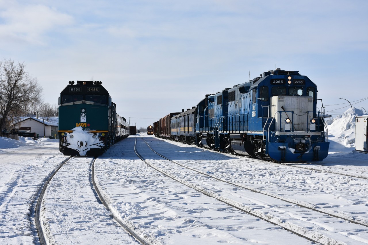 Two's company, three's NOT a crowd! 
VIA 691 is in the siding at left, KRC 291 The Pukatawagan Mixed sits on the main in front of the station, and yard switcher HLCX 3840 is in the distance having just tacked a few cars on the tail end of The Mixed. 
HLCX 3840 is on its way back to the yard near the roundhouse, KRC 291 is just minutes away from departing The Pas, MB for points northwest, and VIA 691 will sit idling for a few more hours until it's time to head north to Churchill, MB. 
Endless railroad action, all day, every day, in The Pas. :-)