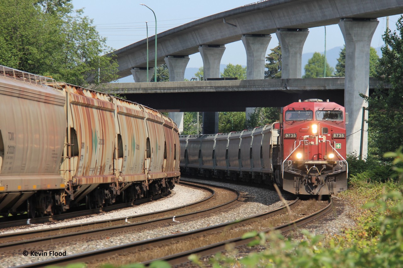 An eastbound potash train led by CP 8735 rounds the bend at Sperling in Burnaby, BC, passing a westbound potash train with CN power waiting to take the tunnel to North Vancouver. Immediately after the front end of the eastbound passed me, another westbound went through the middle track, occupying all three tracks. That train had sulphur loads with CN power. It was a hot few minutes after an almost 1.5 hour lull with only the waiting westbound potash train. June 23, 2023.