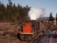On Vancouver Island, Thursday 1976-04-01 was frosty, and G12 CN 991 was left idling overnight at Deerholme to prevent freeze-up, leading to an excessive accumulation of exhaust system deposits.  Well aware of the unpleasant smoke likely to affect the tailend crew, the engineer worked the engine against full-set engine brakes to “clear its throat” on a short run eastward before tying onto the distant pole loads and caboose for a run down to the barge slip at Cowichan Bay.