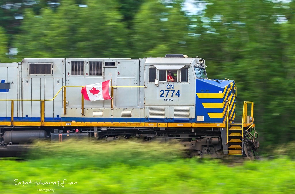 Canada Day 2023. CN 2774 leads train 594 at Passekeag, New Brunswick. Every Canada Day, a buddy of mine, engineer MJR hangs the Canada Flag on the side of his train. This year is the first year I've been able to nab a decent photo of the flag waving in all it's glory, as well as a thumbs up from MJR.