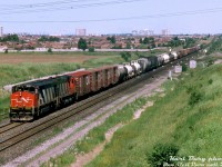 A warm July afternoon in 1993 finds CN HR616 2118 and an M636 rolling train #305 through the interlocking plant at Snider on the York Sub, hammering the diamond with CN's Newmarket Subdivision before taking the inbound leads into the sprawling MacMillan Yard nearby. The twenty 251-powered 2100-series Bombardier HR616's were CN's last dabble into 6-axle Alco/MLW power, and the first CN units to sport the new "Draper Taper" cowl hoods. Future orders would go to GMD (SD50F/SD60F) and later GE (C40-8M) however, and both would outlive the HR616's.
<br><br>
<i>Karl Bury photo, Dan Dell'Unto collection slide.</i>