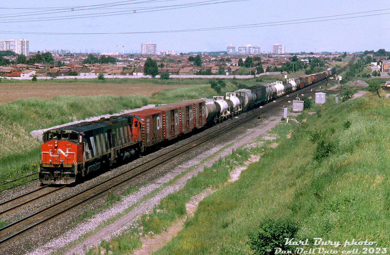 A warm July afternoon in 1993 finds CN HR616 2118 and an M636 rolling train #305 through the interlocking plant at Snider on the York Sub, hammering the diamond with CN's Newmarket Subdivision before taking the inbound leads into the sprawling MacMillan Yard nearby. The twenty 251-powered 2100-series Bombardier HR616's were CN's last dabble into 6-axle Alco/MLW power, and the first CN units to sport the new "Draper Taper" cowl hoods. Future orders would go to GMD (SD50F/SD60F) and later GE (C40-8M) however, and both would outlive the HR616's.

Karl Bury photo, Dan Dell'Unto collection slide.